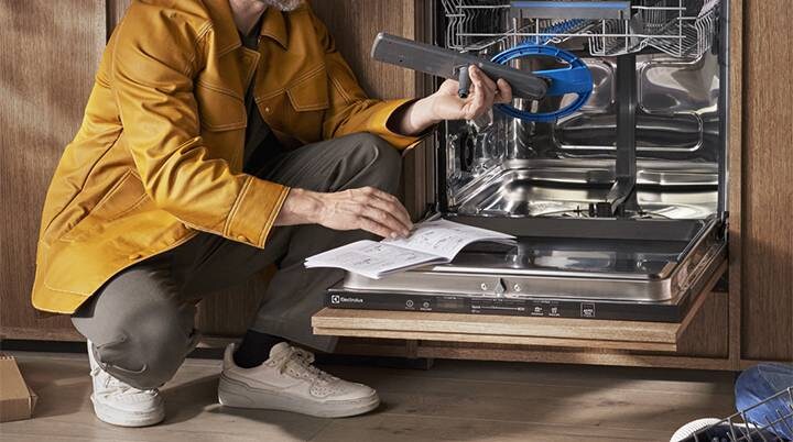 Person in front of open dishwasher readin user manual