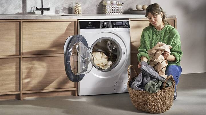 Woman in green with laundry basket in front of open washing machine