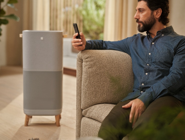 Mężczyzna trzymający telefon, siedzący obok oczyszczacza powietrza.