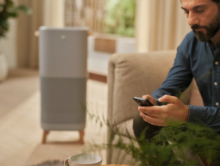 Mężczyzna trzymający telefon, siedzący obok oczyszczacza powietrza.