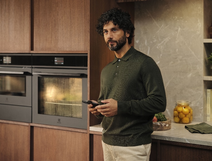 Mężczyzna stojący w kuchni z telefonem w ręku